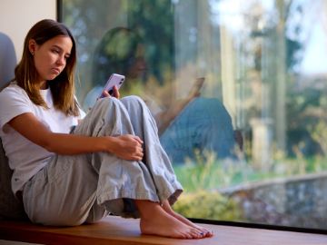 Mädchen sitzt am Fenster und schaut ins Handy